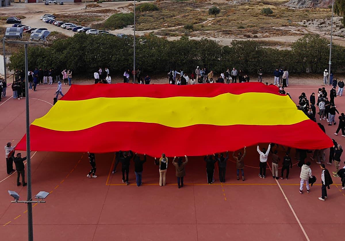 Alumnos y profesores del instituto Bartolomé Pérez Casas despliegan la bandera de España en el patio del centro.
