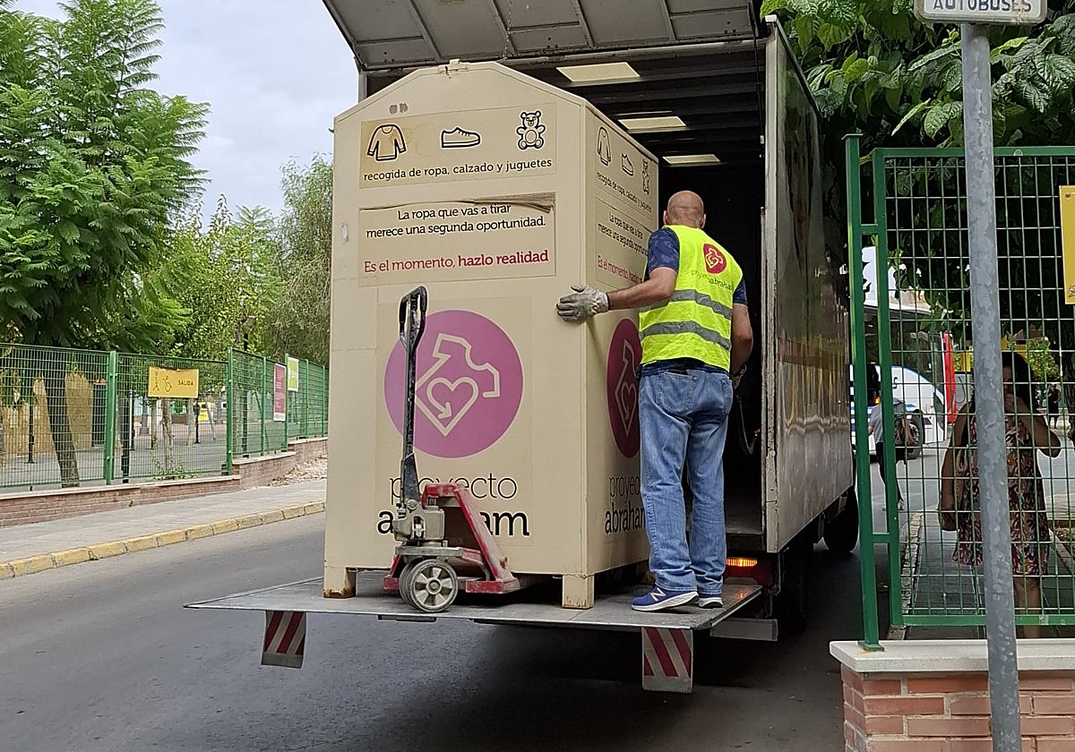 Un operario retira uno de los contendores de recogida de ropa usada.