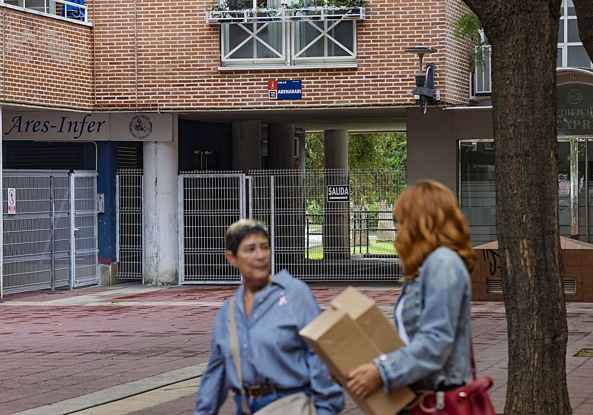 Dos viandantes pasan frente a el entorno vallado bajo el edificio Capri, junto a la calle Abenarabi.