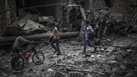 Tres niños caminan entre los escombros.