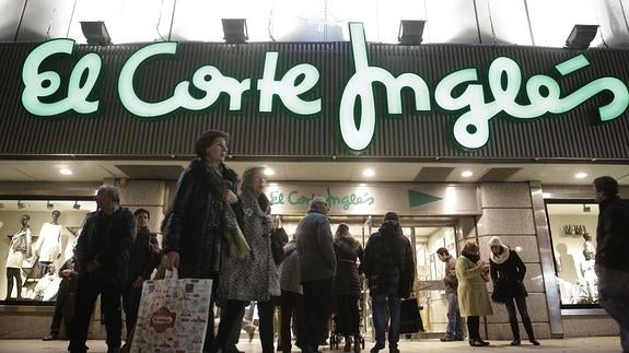 Varias personas con bolsas de las compras de Navidad, junto a El Corte Ingles.