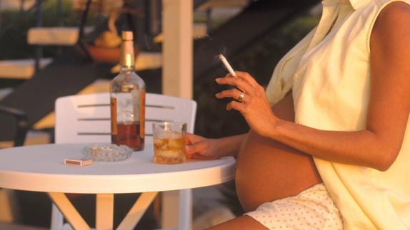 Una mujer embarazada fuma y bebe.
