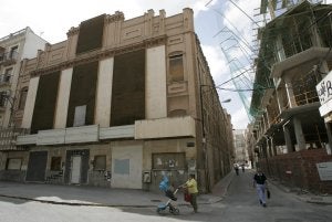 Una mujer pasa con un carricoche pasa frente al antiguo Cine Central, a la izquierda, y el edificio en construcción en la calle Don Roque. ::                             J. M. RODRÍGUEZ / AGM