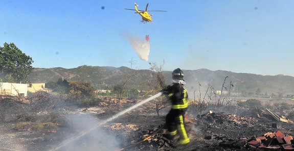 Un bombero trabaja en la extinción del fuego mientras un helicóptero vacía el depósito de agua. A la derecha, una vecina asustada por el siniestro. 