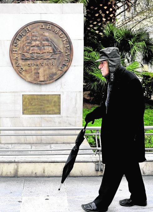 Un viandante pasa junto a un monumento en el centro de Atenas, en el que aparece una representación del antiguo dracma. 