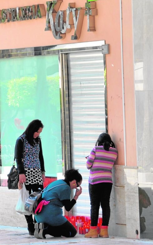 Una mujer no puede contener las lágrimas mientras coloca una vela en presencia de dos jóvenes a las puertas de la pastelería Katy de Águilas, que regentaba Fernando Martínez.