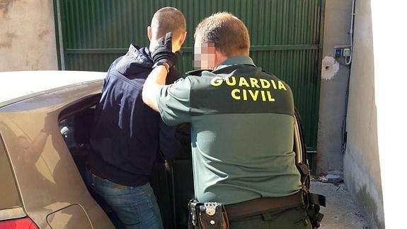 Un agente de la Guardia Civil introduce a uno de los detenidos en el vehículo para su traslado. 