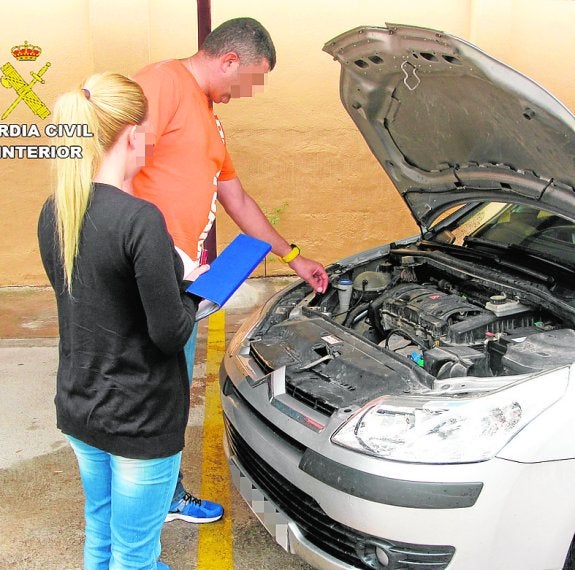 Dos investigadores de la Guardia Civil inspeccionan el motor de uno de los vehículos comerciales de la empresa estafada. 