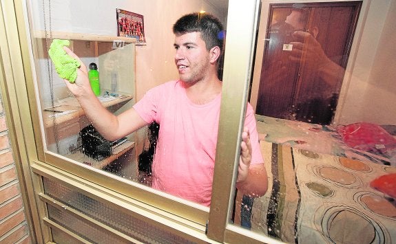 Adrián López limpia las ventanas de su cuarto, en el piso tutelado de Astrapace en el que vive..