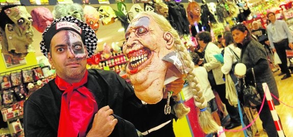 Un hombre disfrazado muestra una máscara, mientras los clientes hacen cola en una tienda de disfraces, ayer. 