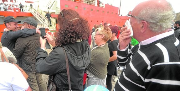 Un tripulante del buque se abraza a un familiar, entre otros emocionados por la llegada a casa. 