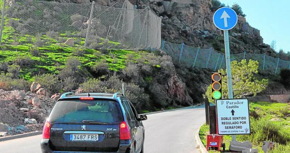 Un vehículo inicia su marcha tras ponerse en verde el semáforo que regula el doble sentido de la carretera de acceso al castillo, tras clausurarse la de bajada. 