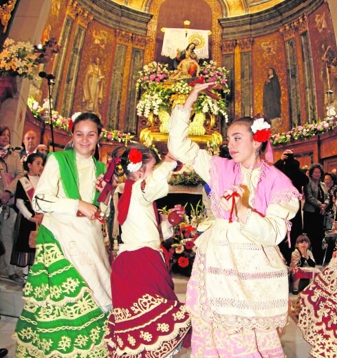 Tres chicas bailan y tocan las castañuelas, en la Basílica de la Caridad, frente al altar mayor y a la Patrona.