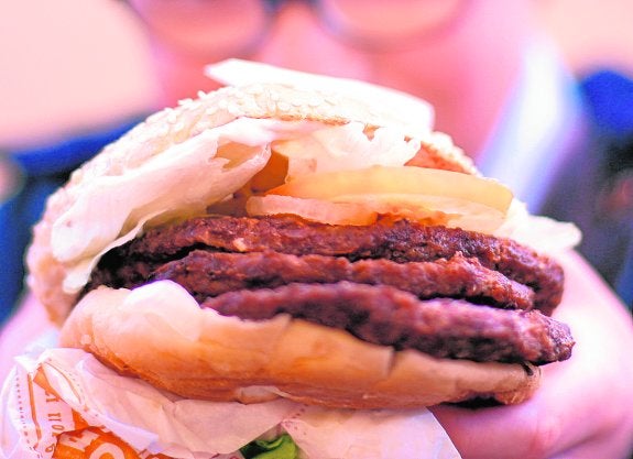 Un adolescente come una hamburguesa triple en un establecimiento de comida rápida. 