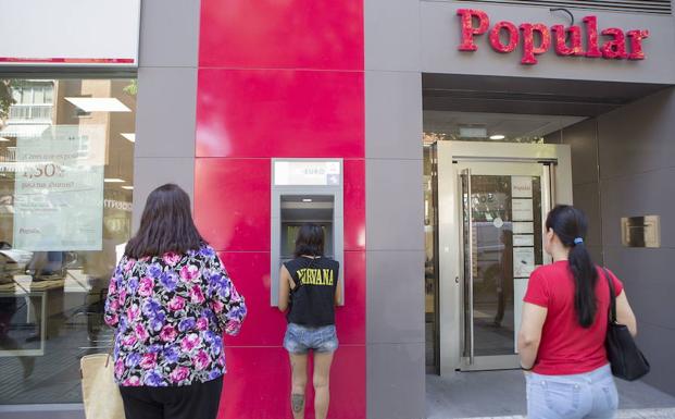 Clientes sacan dinero del cajero de una oficina del Banco Popular en Madrid. 