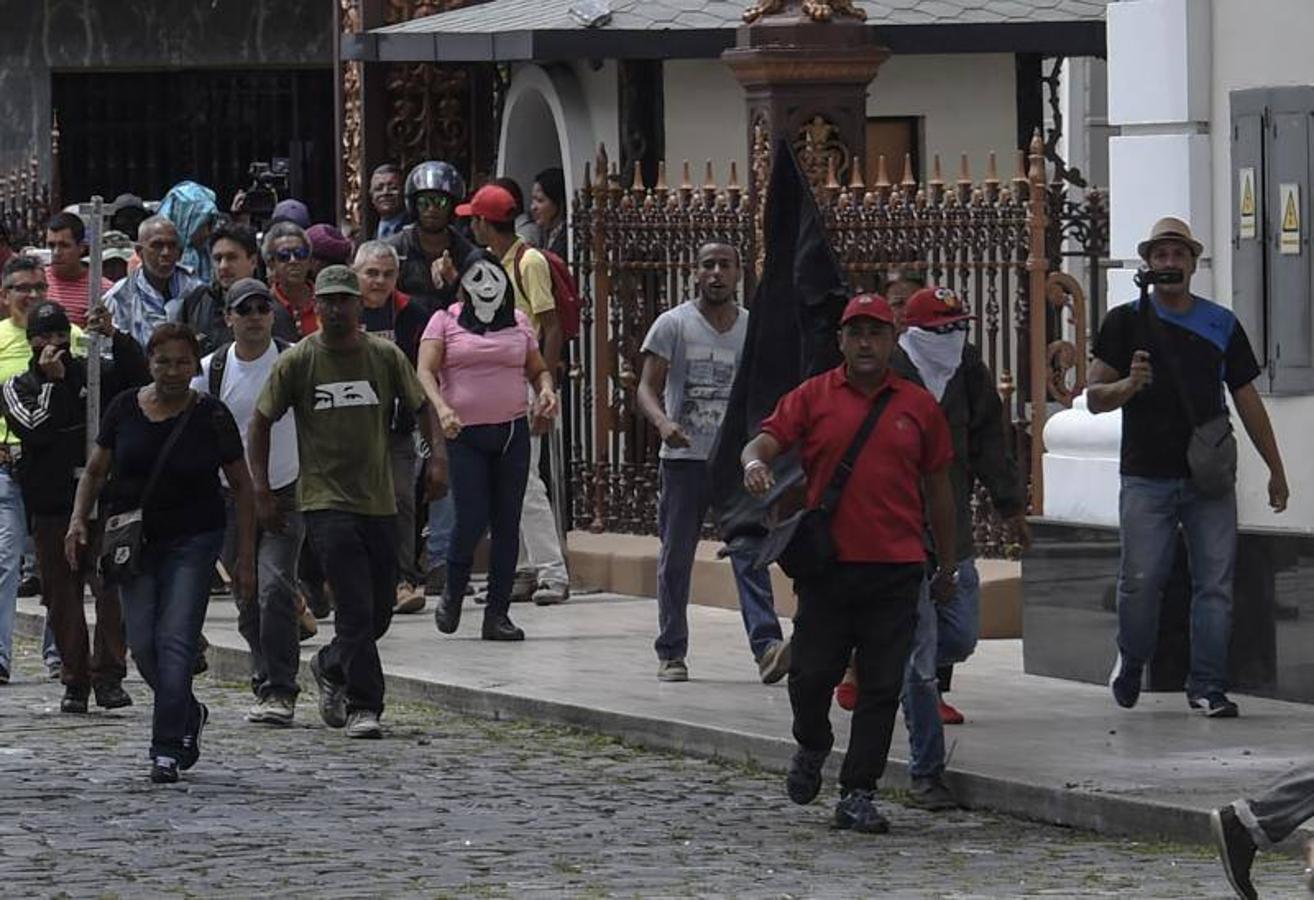 Decenas de personas, algunas encapuchadas, con palos y tubos, y vestidas de rojo, entraron a los jardines de la Asamblea Nacional y detonaron cohetes de fuegos artificiales, desatando el caos