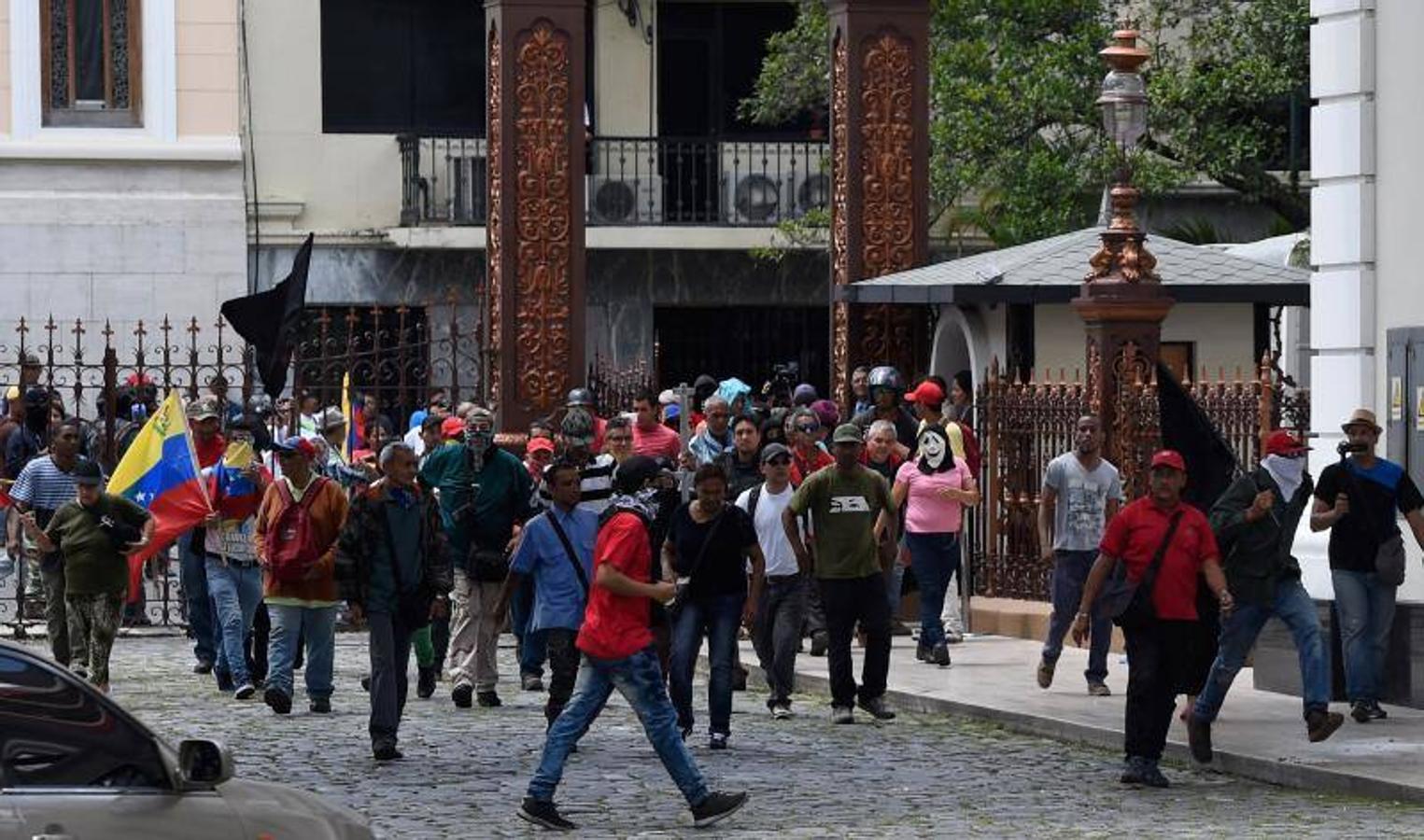 Decenas de personas, algunas encapuchadas, con palos y tubos, y vestidas de rojo, entraron a los jardines de la Asamblea Nacional y detonaron cohetes de fuegos artificiales, desatando el caos