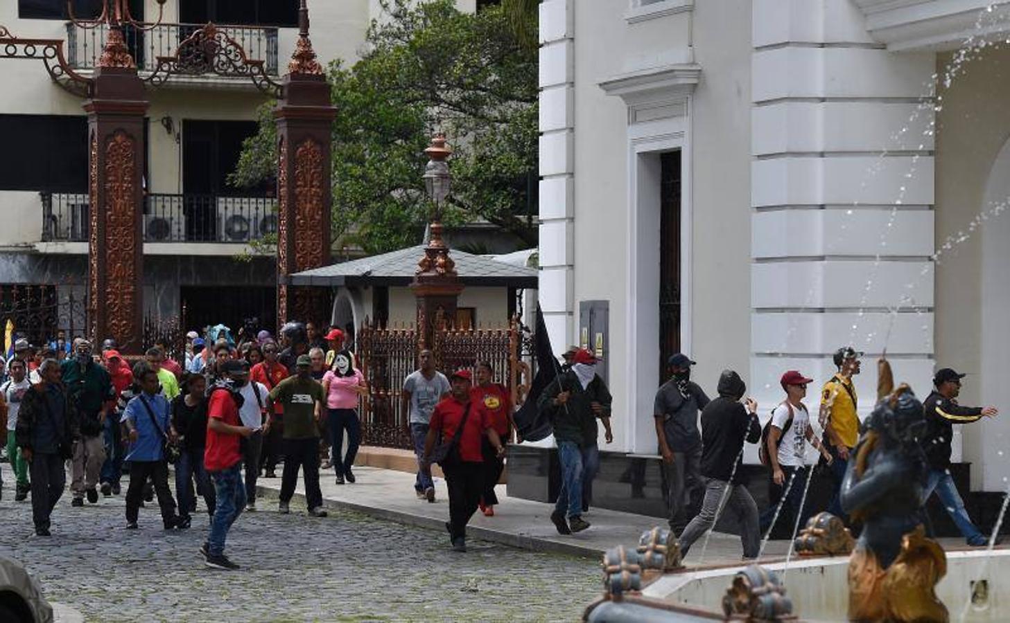 Decenas de personas, algunas encapuchadas, con palos y tubos, y vestidas de rojo, entraron a los jardines de la Asamblea Nacional y detonaron cohetes de fuegos artificiales, desatando el caos