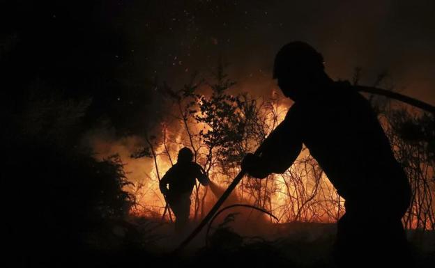 Bomberos y brigadas forestales de la Xunta de Galicia apagan en las proximidades de Santiago de Compostela un incendio forestal. 