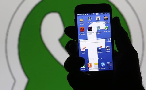 Un usuario sostiene un móvil con el logo de Facebook en la pantalla, ante el icono de Whatsapp.
