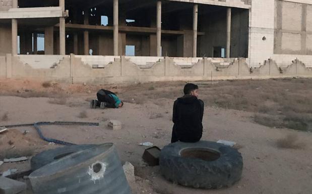 Dos hombres rezan mientras esperan la llegada del resto de evacuados civiles y combatientes de Faylaq al-Rahman, a las afueras de Damasco (Siria), para salir de la población de Duma hacia Idlib. 