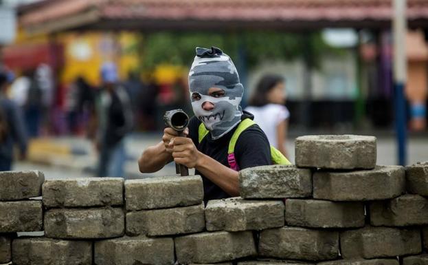 Un joven con la cara tapada y un arma posa para una fotografía en una barricada en el barrio indígena de Monimbó. 