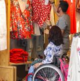 Un asistente personal acompaña a comprar ropa a una mujer en silla de ruedas.