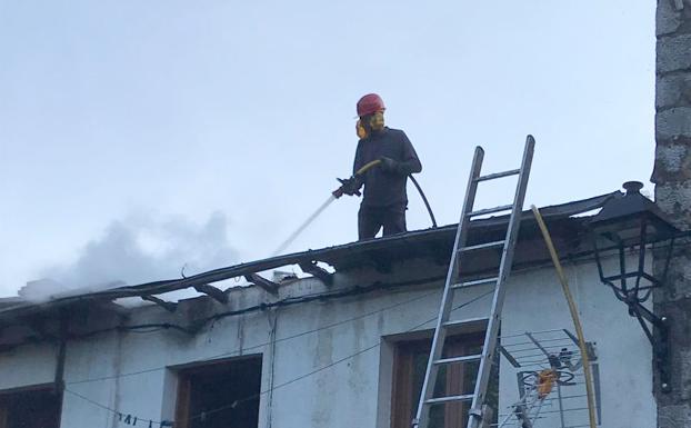 Un vecino, en el techo de una casa, intenta sofocar el fuego usando una manguera.