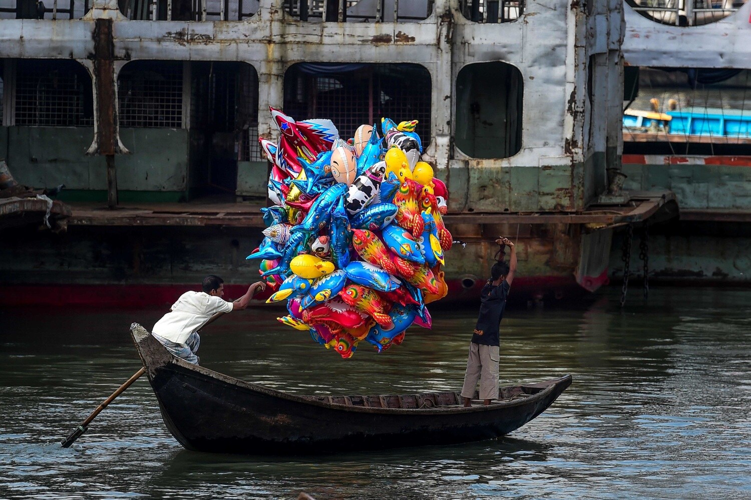 Un hombre sostiene globos mientras cruza el río Buriganga en un bote en Dhaka, Bangladés