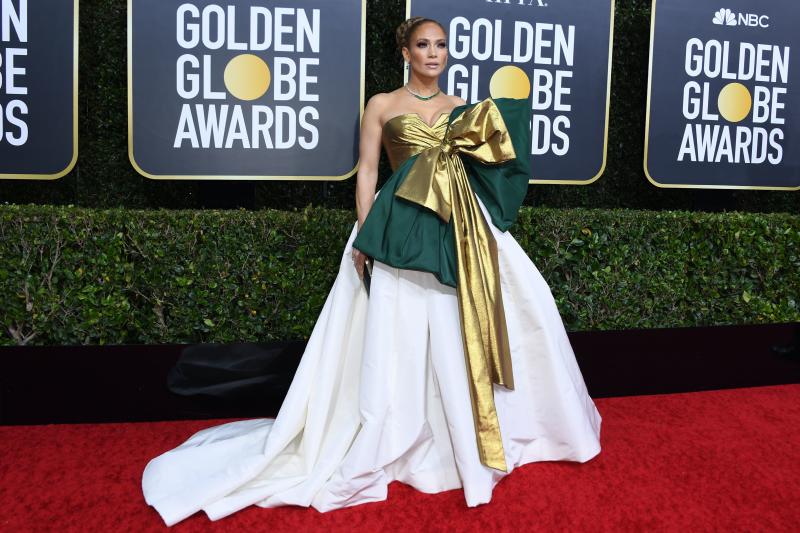 Jennifer Lopez deslumbra con un vestido de escote drapeado palabra de honor en dorado del que sale un maxi lazo también en dorado superpuesto sobre uno verde y falda blanca de princesa