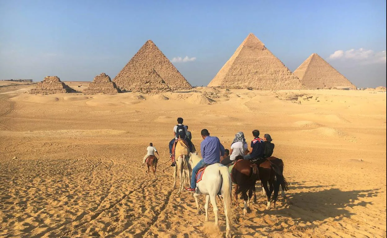 Un grupo de turistas se dirige en caballo a las pirámides de Egipto.