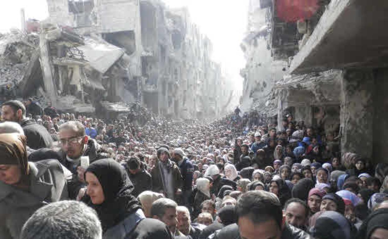 Cientos de personas hacen cola en el campamento de Al Yarmouk, Damasco, para recibir alimentos de la ayuda humanitaria de Naciones Unidas en 2014 