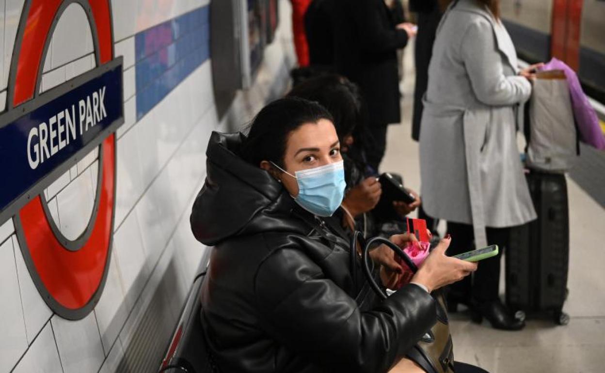 Una joven se protege con una mascarilla mientras espera el metro, en Londres.