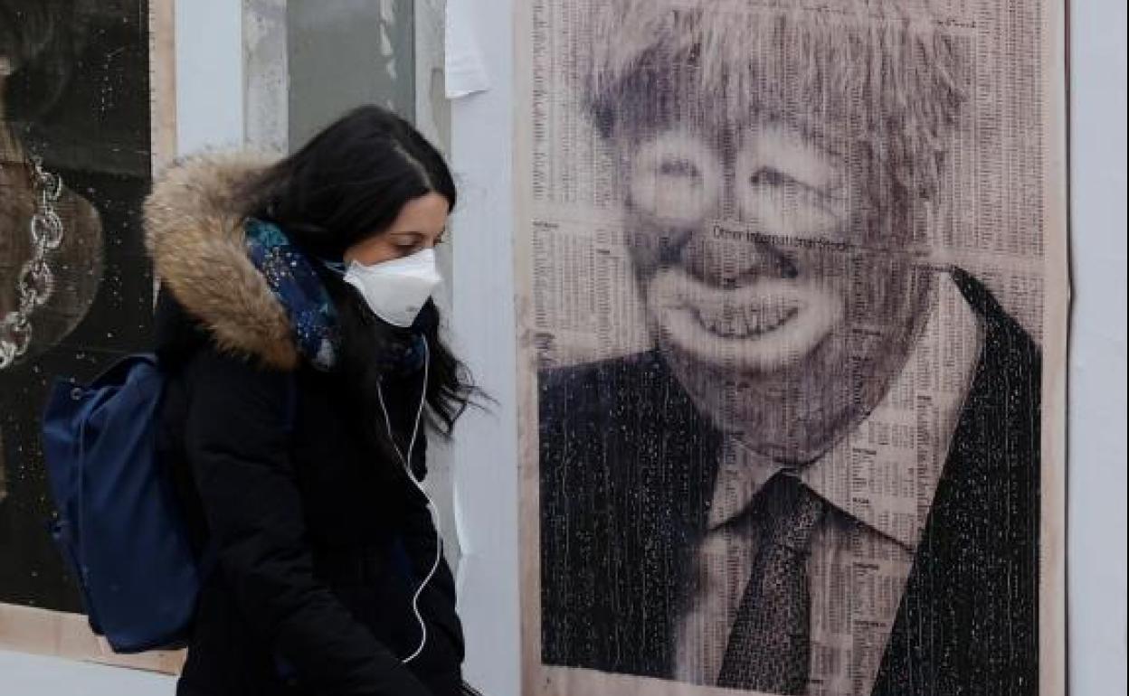 Una mujer con mascarilla pasa ante un cartel crítico con Boris Johnson, en Mánchester.