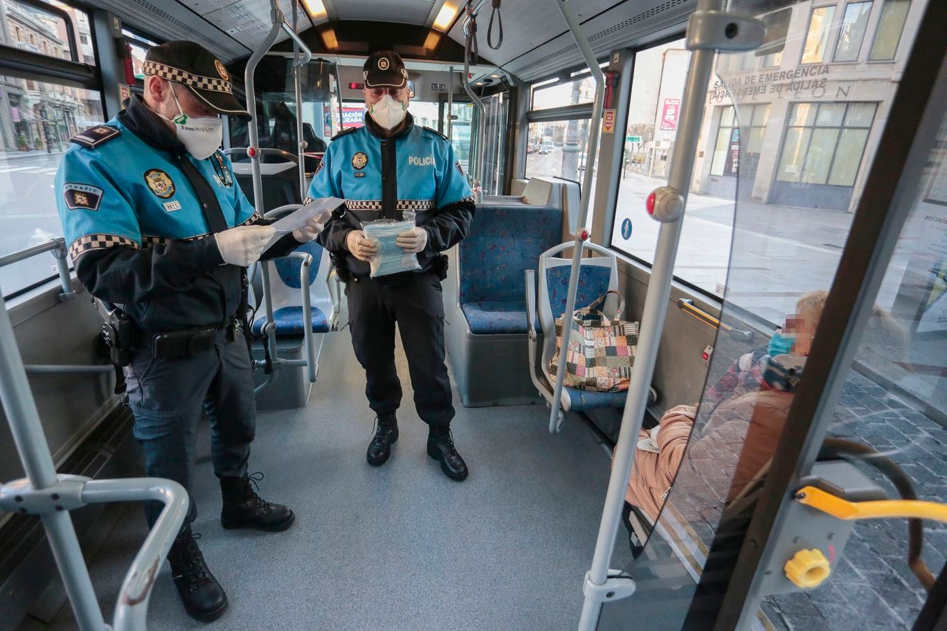 Miembros de Policía Local, Policía Nacional y Protección Civil de León, reparten mascarillas a usuarios del transporte público.
