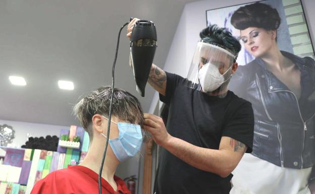 El peluquero protegido con mascarilla y pantalla con el uso del secador. 