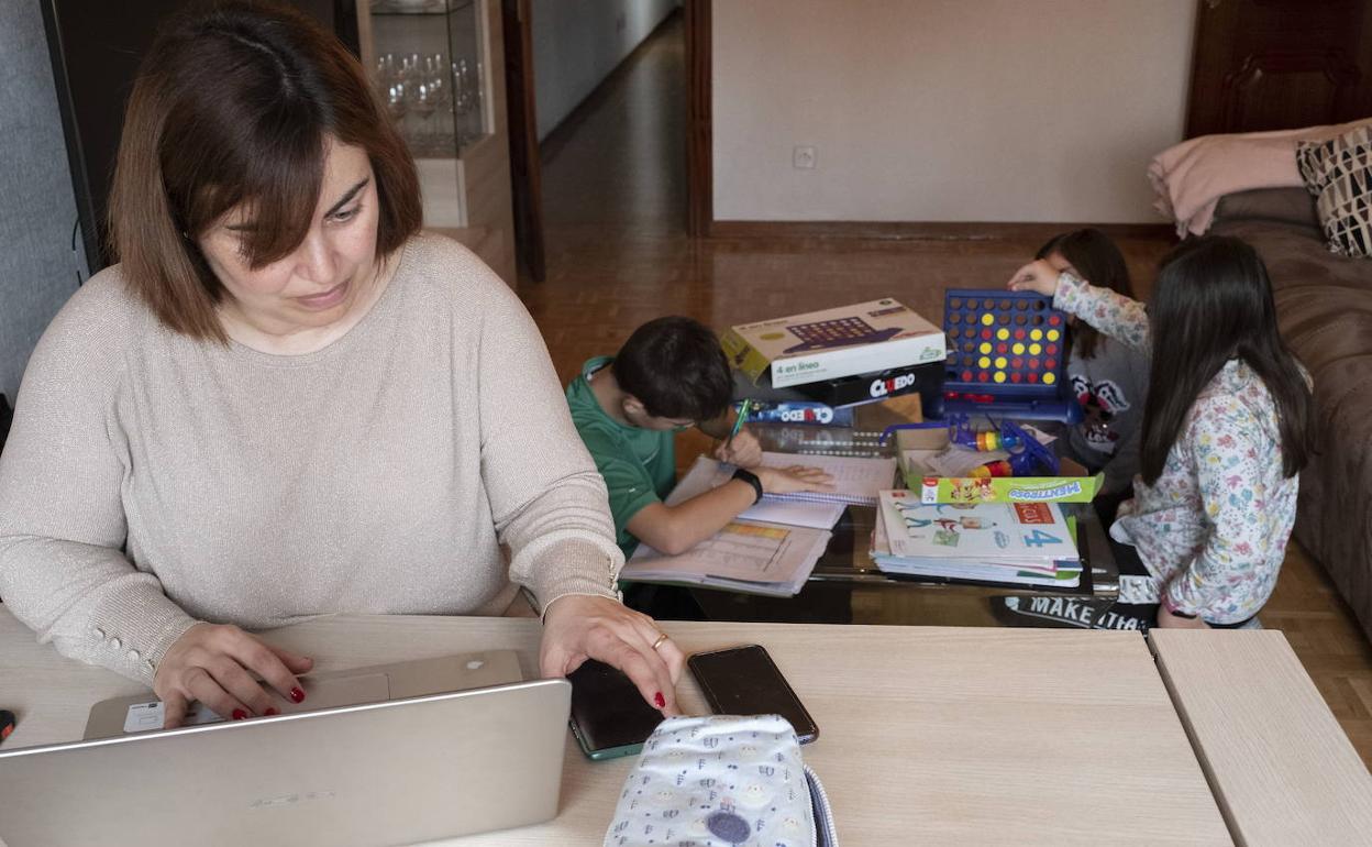 Una madre trabaja desde casa mientras sus hijos estudian al lado. 