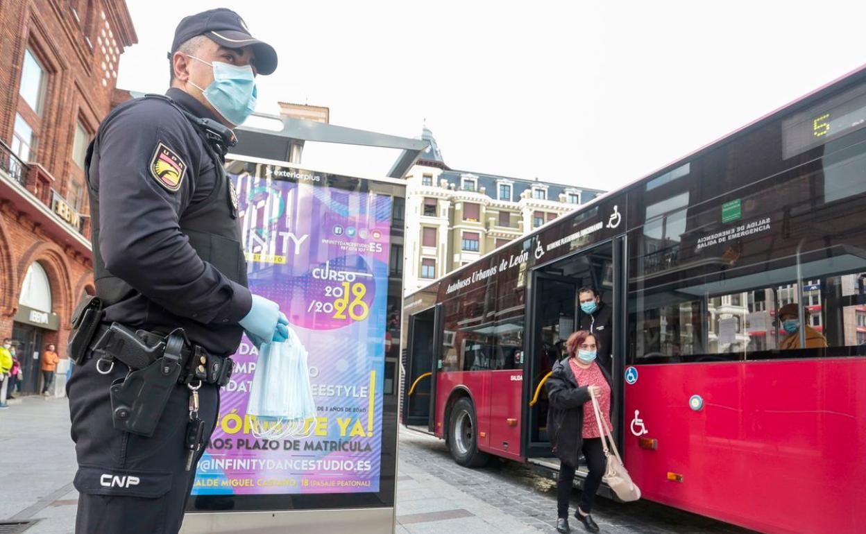 Un miembro de la Policía Nacional entrega mascarillas junto a un bus urbano de León capital. 