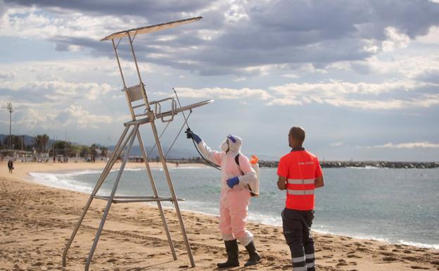 Unos trabajadores desinfectan los puestos de socorrismo en la playa del Bogatell, en Barcelona. 