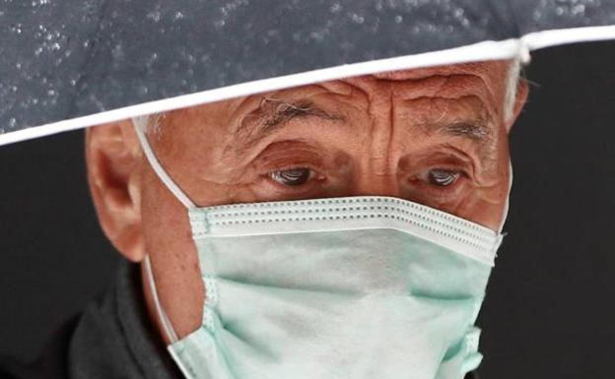 Un hombre pasea bajo la lluvia con mascarilla.