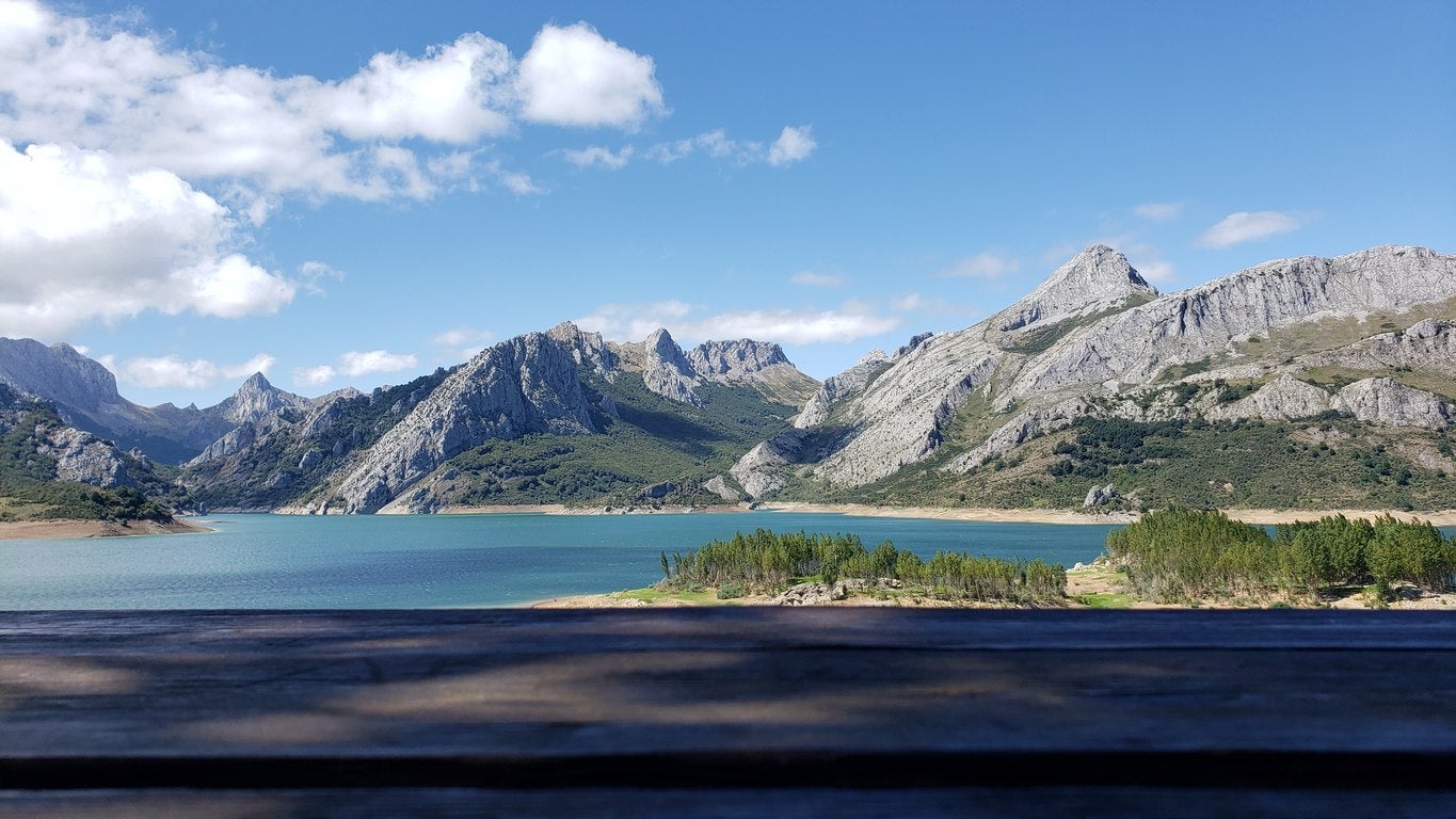 Ubicado junto a la Ermita de Nuestra Señora, en Riaño, el banco ofrece unas privilegiadas vistas sobre el pantano y Picos | El entorno, con las viejas campanas y un 'horreo leonés', completa un escenario idílico. 