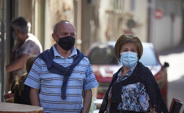 Un hombre y una mujer con mascarilla pasean por una calle.