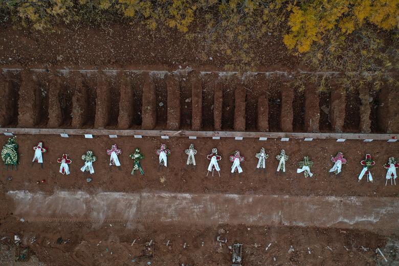 Se colocan coronas de flores en tumbas junto a tumbas recién abiertas, en un área de cementerio designada para pacientes que murieron por el coronavirus en Salónica, Grecia.