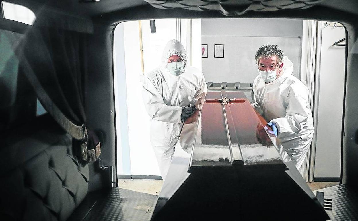 Dos empleados de una funeraria preparan el sepelio de una persona fallecida en Portugal por la epidemia. 