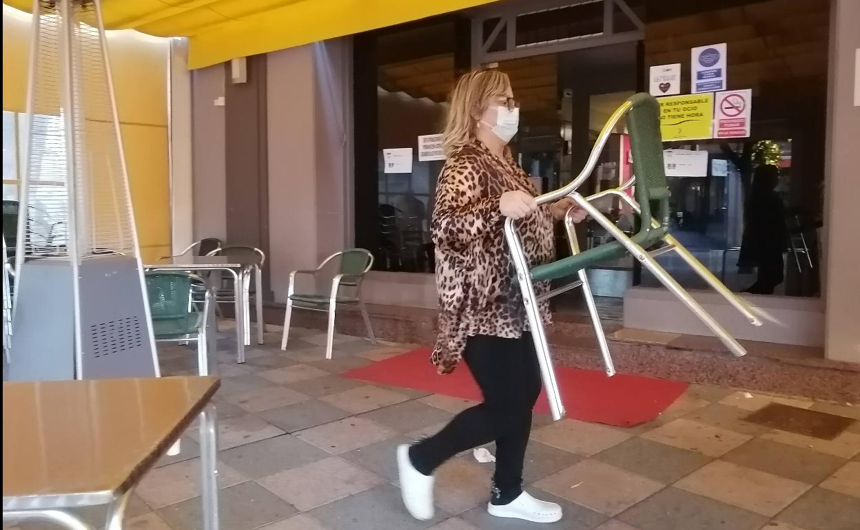 Una mujer recoge su terraza a las seis de la tarde, cuando debía cerrar su establecimiento.