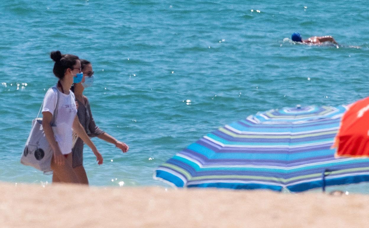 Dos mujeres pasean por la playa con sus respectivas mascarillas. 