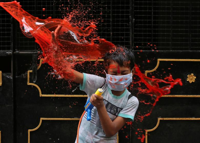 Un niño con una mascarilla protectora reacciona cuando lo bañan con agua coloreada durante las celebraciones de Holi en Chennai, India.