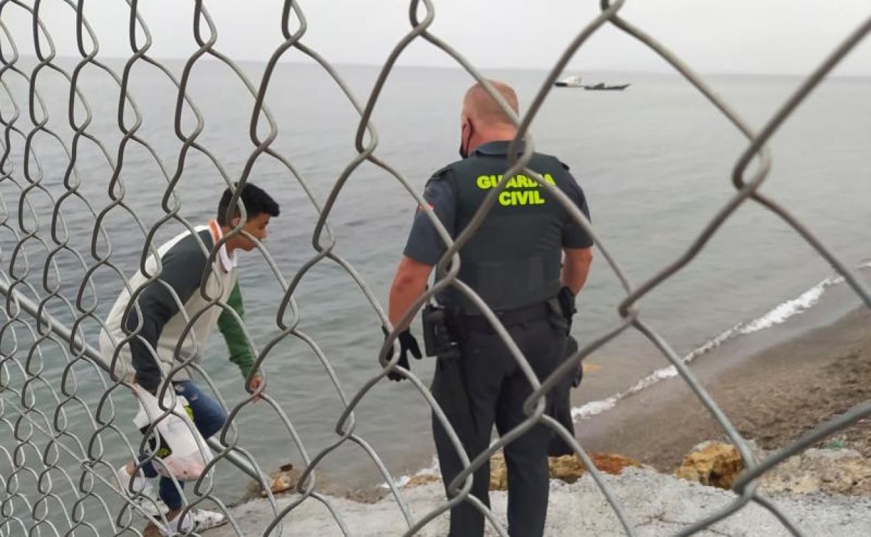 Un Guardia Civil ayuda a uno de los inmigrantes en uno de los espigones fronterizos de Ceuta 