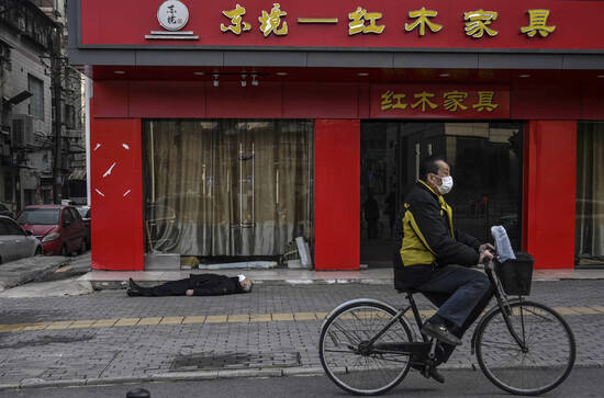 Un ciclista pasa junto al cadáver de un fallecido en Wuhan. 