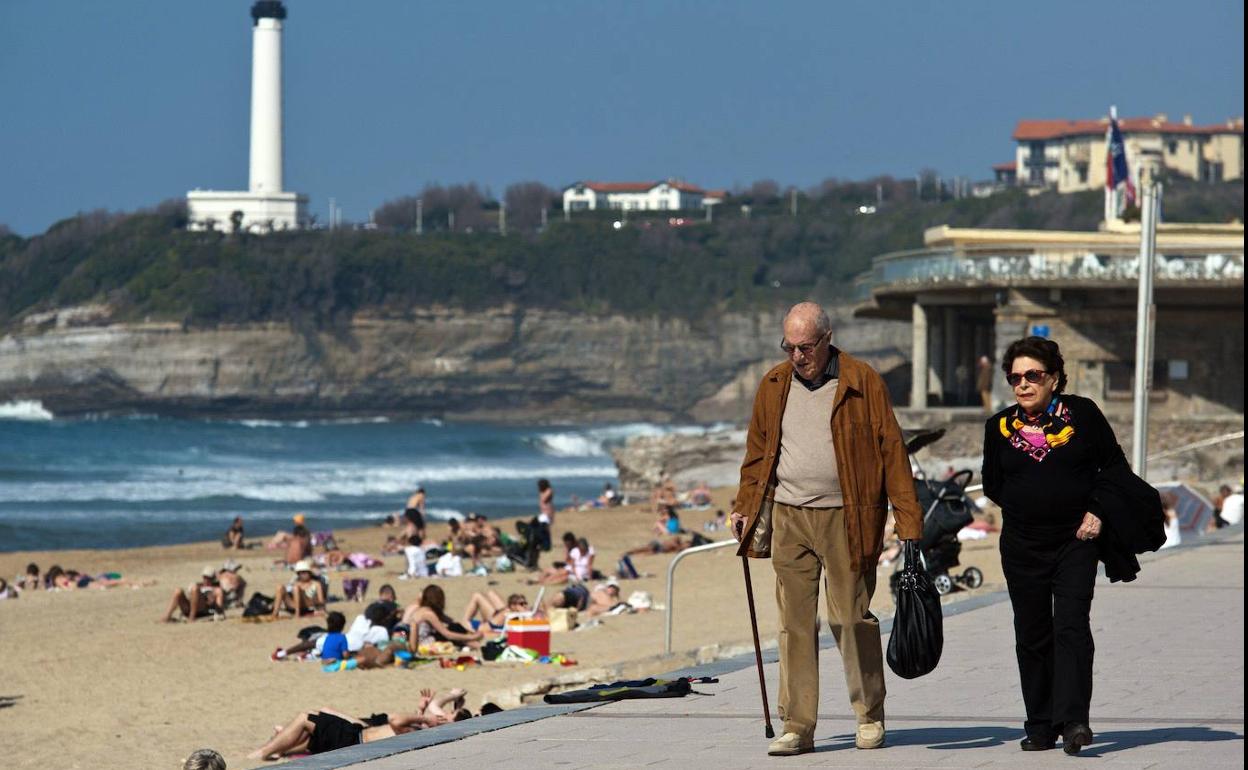 Dos jubilados paseando frente a una playa. 